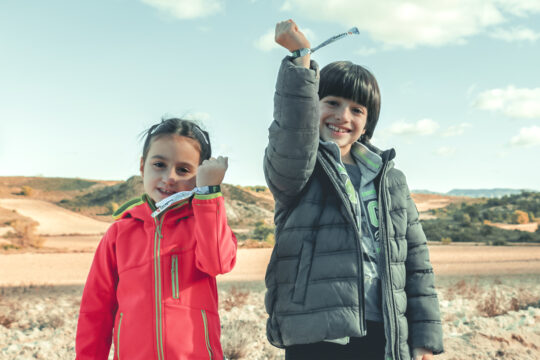 Dos niños con el brazo en alto mostrando las pulseras del Bosque de los Zaragozanos