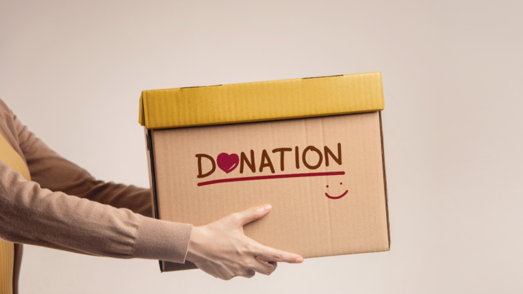 Se ve el torso y los brazos de una persona ofreciendo una caja cn el texto DONATION